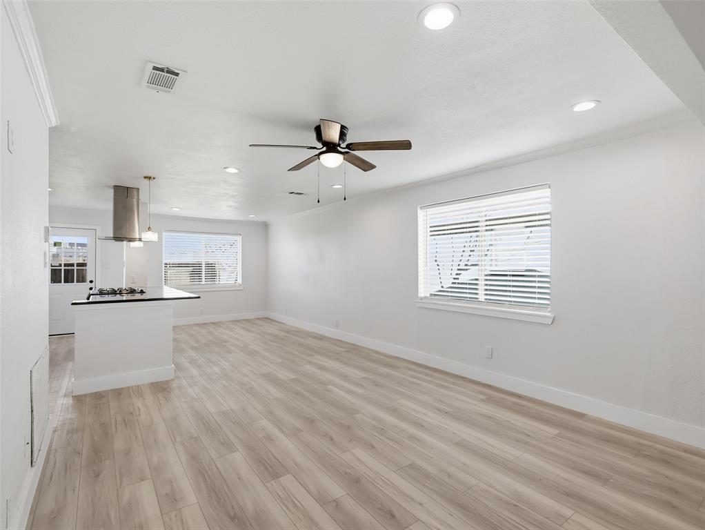 Open interior featuring wood-finish flooring, recessed lighting, a ceiling fan, and a kitchen island with a stone countertop and stainless steel range hood Open interior featuring wood-finish flooring, recessed lighting, a ceiling fan, and a kitchen island with a stone countertop and stainless steel range hood