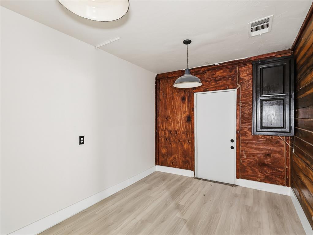 Interior space featuring wood-finish flooring, exposed wood-paneled walls, a single-bulb dome pendant light, and a black-framed window fixture