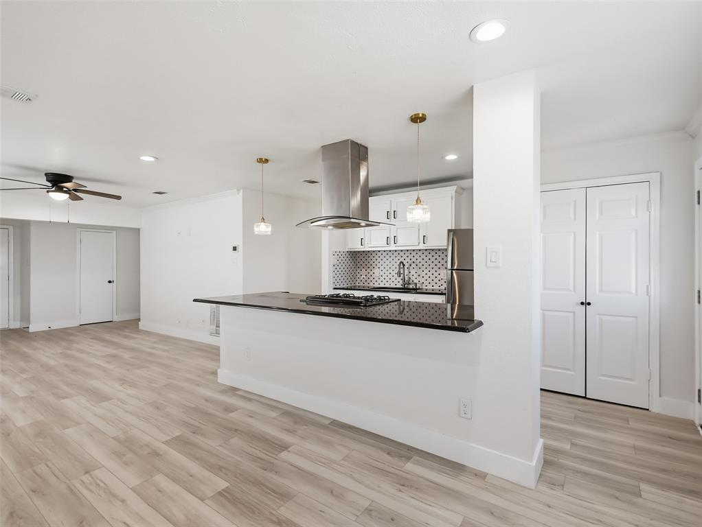 Kitchen featuring wood-finish flooring, dark stone countertops, stainless steel chimney-style range hood, patterned tile backsplash, and dual pendant lighting