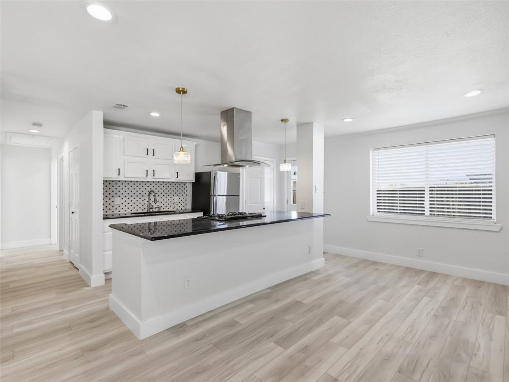 Kitchen featuring a stone-surface island, white cabinetry, a patterned tile backsplash, stainless steel range hood, and wood-finish flooring