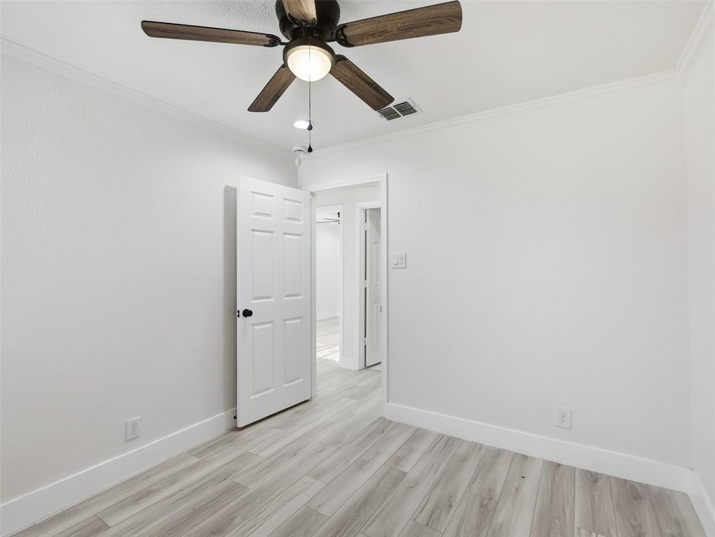 Interior room featuring wood-finish flooring, a multi-blade ceiling fan with integrated light fixture, and a six-panel door