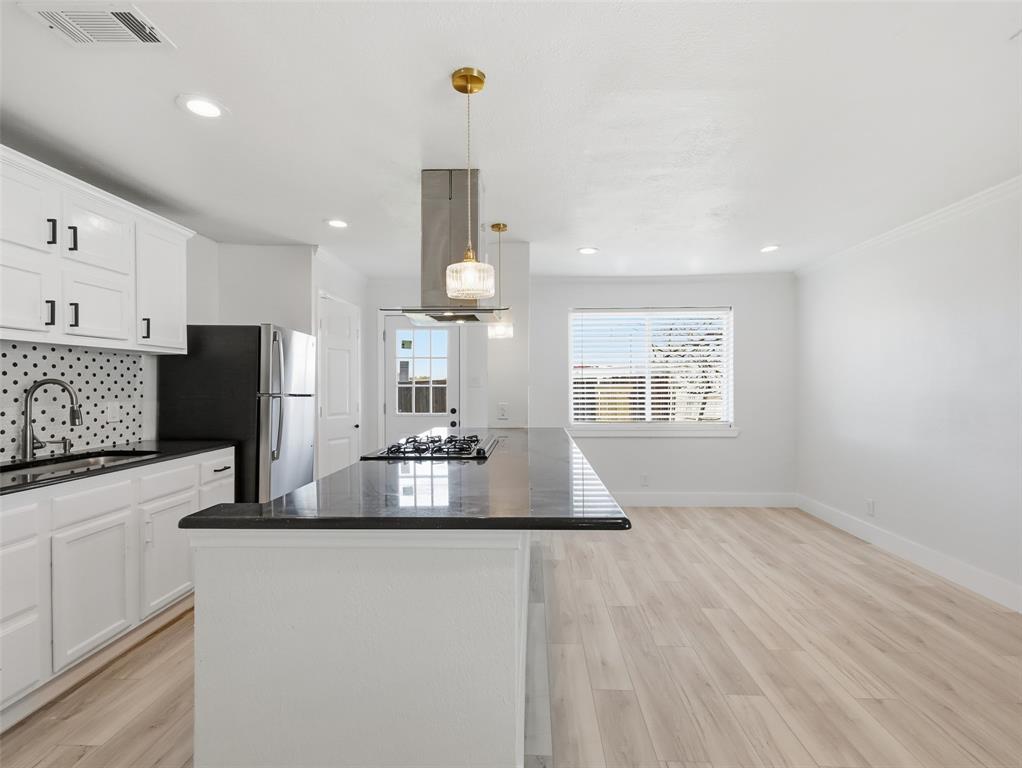 Kitchen featuring white shaker-style cabinetry, dark stone-surface countertops, a center island with an integrated gas cooktop, patterned tile backsplash, and recessed lighting Kitchen featuring white shaker-style cabinetry, dark stone-surface countertops, a center island with an integrated gas cooktop, patterned tile backsplash, and recessed lighting