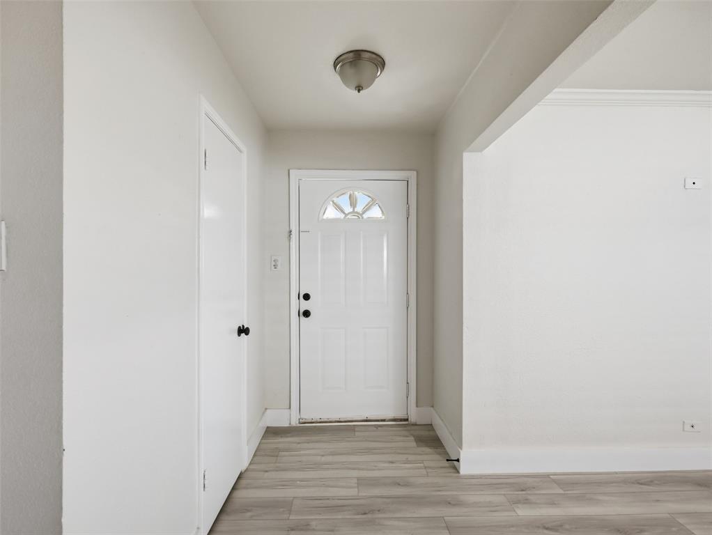 Entryway featuring wood-finish flooring, a six-panel door with a half-moon light, and a flush-mount ceiling fixture Entryway featuring wood-finish flooring, a six-panel door with a half-moon light, and a flush-mount ceiling fixture