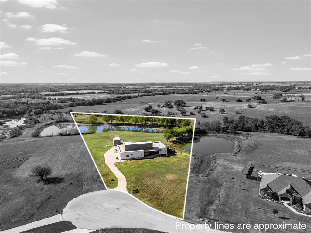 Aerial view of a sprawling property featuring a modern residence, two stock ponds, a concrete driveway, and expansive acreage