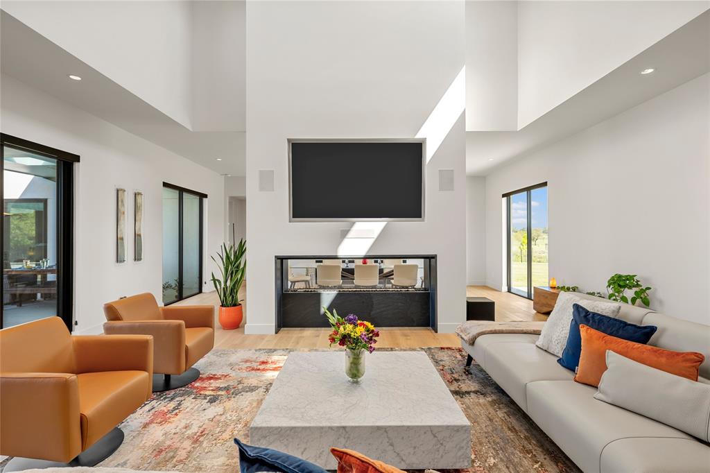 Double-height ceilings featuring recessed lighting, Large glass sliding doors, and a central dual-sided linear fireplace with surround sound throughout.