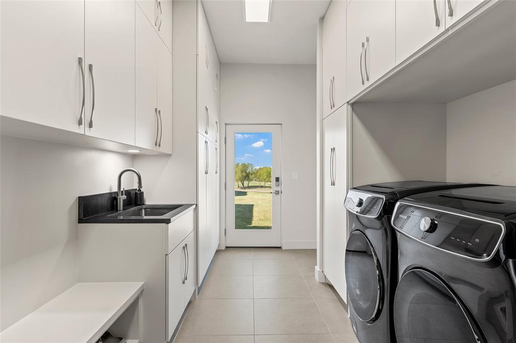 Utility room featuring floor-to-ceiling white cabinetry, Quartzite surface countertop with undermount sink, sleek metal hardware, and 24 inch tile flooring
