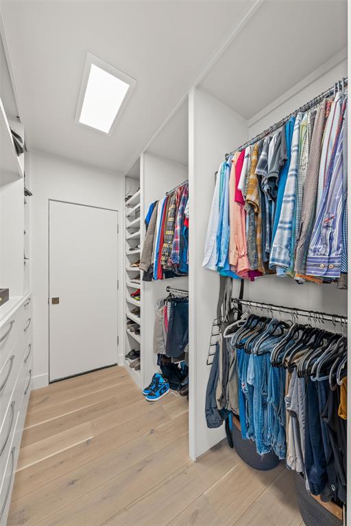Walk-in 2-sided closet featuring custom white built-in shelving, multi-level hanging rods, integrated drawer storage, wood-finish flooring, and a recessed ceiling light with mechanical storage and potential safe room