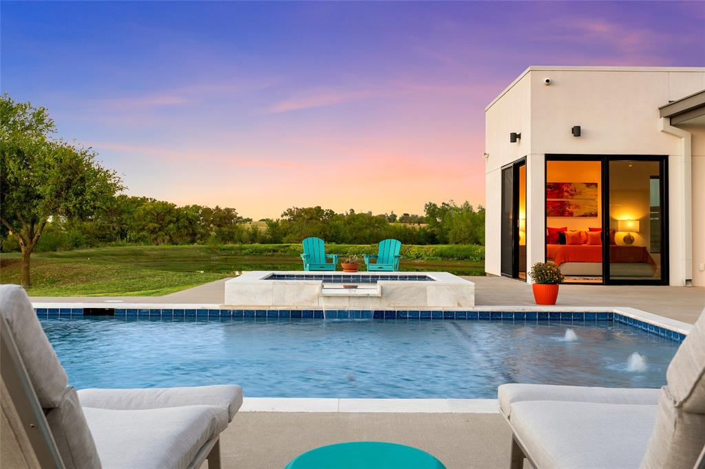 Stucco exterior residence featuring an in-ground pool, elevated spa with spillway, concrete patio, and large-format sliding glass doors