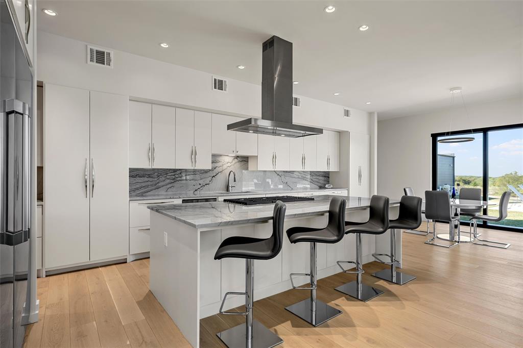 Gourmet kitchen featuring flat-panel cabinetry, a spacious center island with Quartzite countertops, a stainless steel range hood, and wood flooring