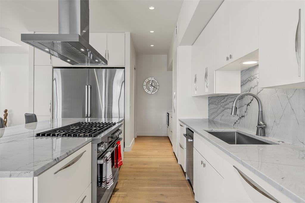 Kitchen featuring flat-panel cabinetry, Quartzite countertops with matching backsplash, Dacor kitchen package with gas range, and wood flooring