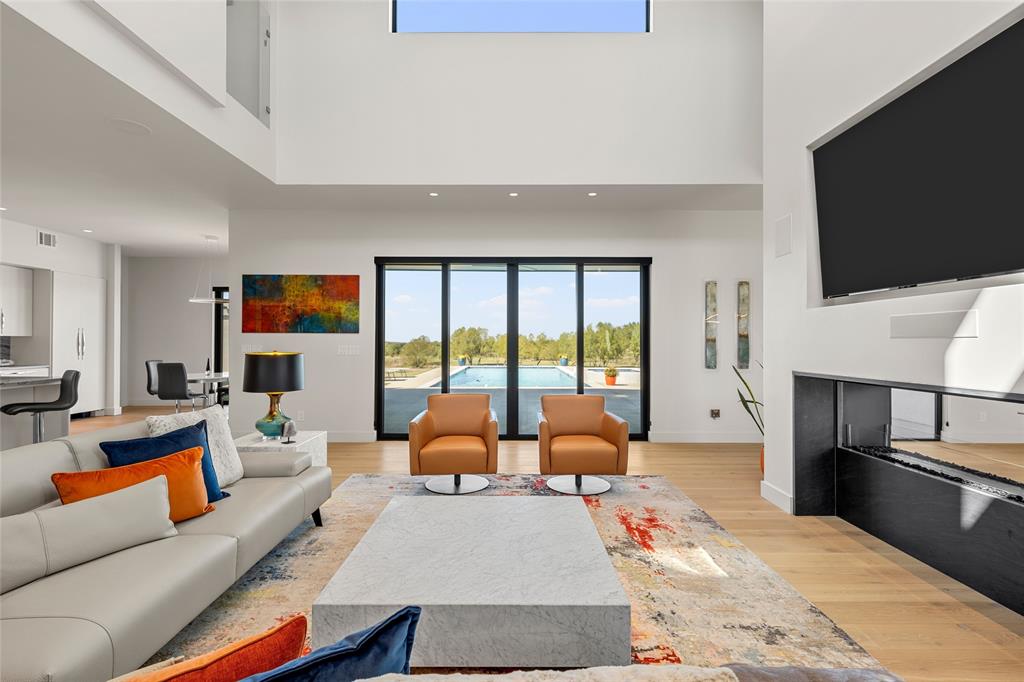 Double-height ceilings with recessed lighting, floor-to-ceiling multi-panel sliding glass doors, built-in linear ethanol fireplace, and wood flooring