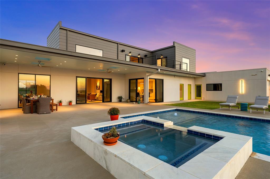 Contemporary exterior featuring a covered patio, integrated pool and spa with stone-style coping, and expansive sliding glass doors