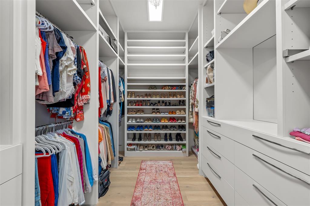 Custom walk-in 2-sided closet featuring floor-to-ceiling white cabinetry, integrated open shelving, wood flooring, and recessed lighting.  Chandelier is excluded from sale
