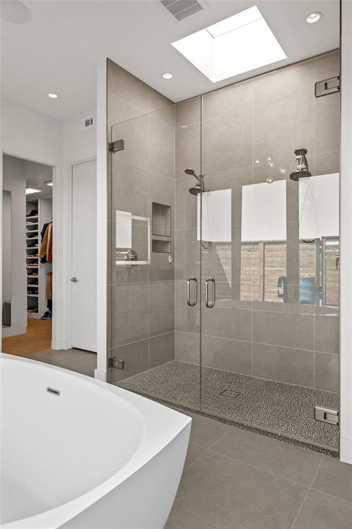 Walk-in shower featuring a frameless glass enclosure, ceiling skylight, dual-head shower system, recessed shelving, and a textured stone-finish floor