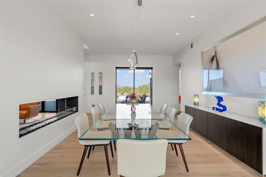 Modern dining space featuring wood flooring, recessed lighting, a linear built-in fireplace, a suspended architectural light fixture, and expansive glass sliding doors