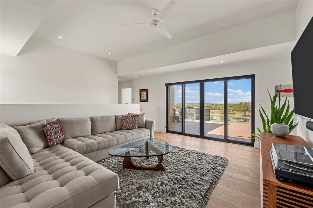 Living area featuring high tray ceilings, wood-flooring, recessed lighting, a modern ceiling fan, and large-format sliding glass doors. Open to living room with clear safety glass and private pocket doors.