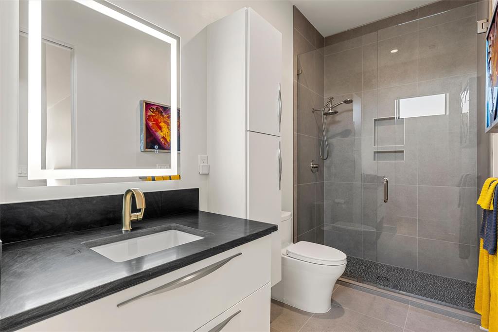 Modern bathroom featuring an integrated LED-lighted mirror, Quartzite vanity countertop with an undermount sink, ample storage, and a walk-in shower with custom tile work surround and a recessed shampoo niche