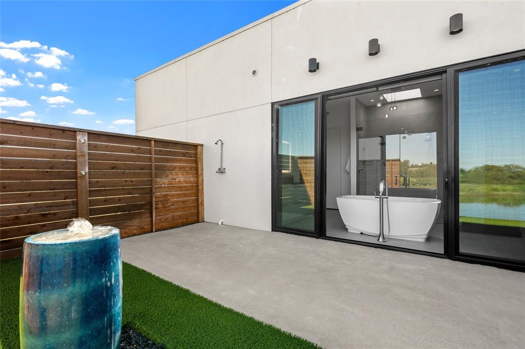 Private patio featuring concrete flooring, a horizontal wood privacy fence, a built-in outdoor shower, and a decorative ceramic water feature