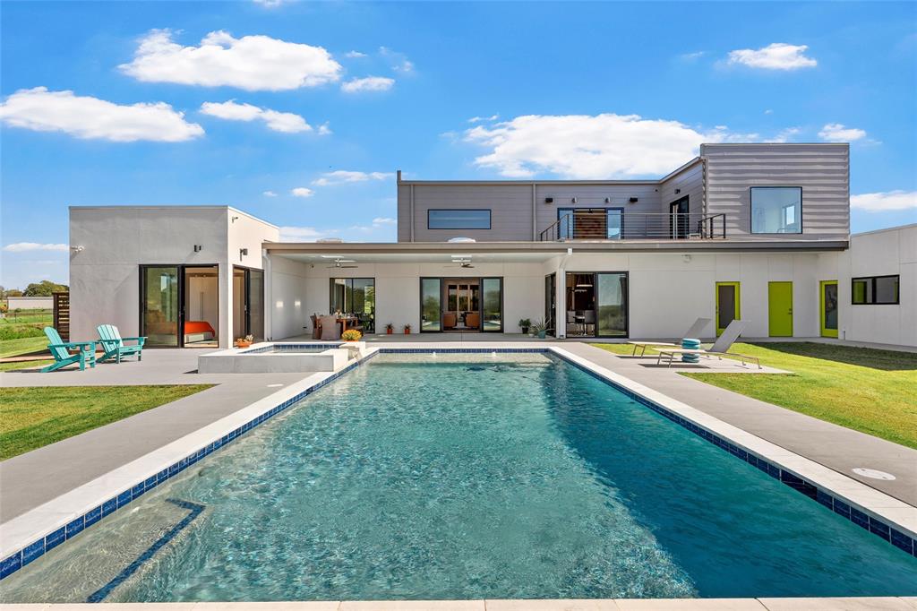 Contemporary multi-level exterior featuring a rectangular inground pool with an integrated spa, expansive covered patio with skylights, second-story balcony with metal railing, and sleek mixed-material siding