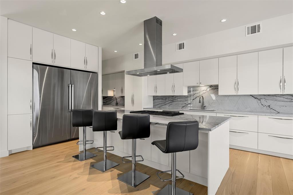 Kitchen featuring white cabinetry, Quartzite countertops with matching backsplash, Dacor 36 inch refrigerator and 36 inch freezer, center island with built-in Dacor cooktop, and wood flooring