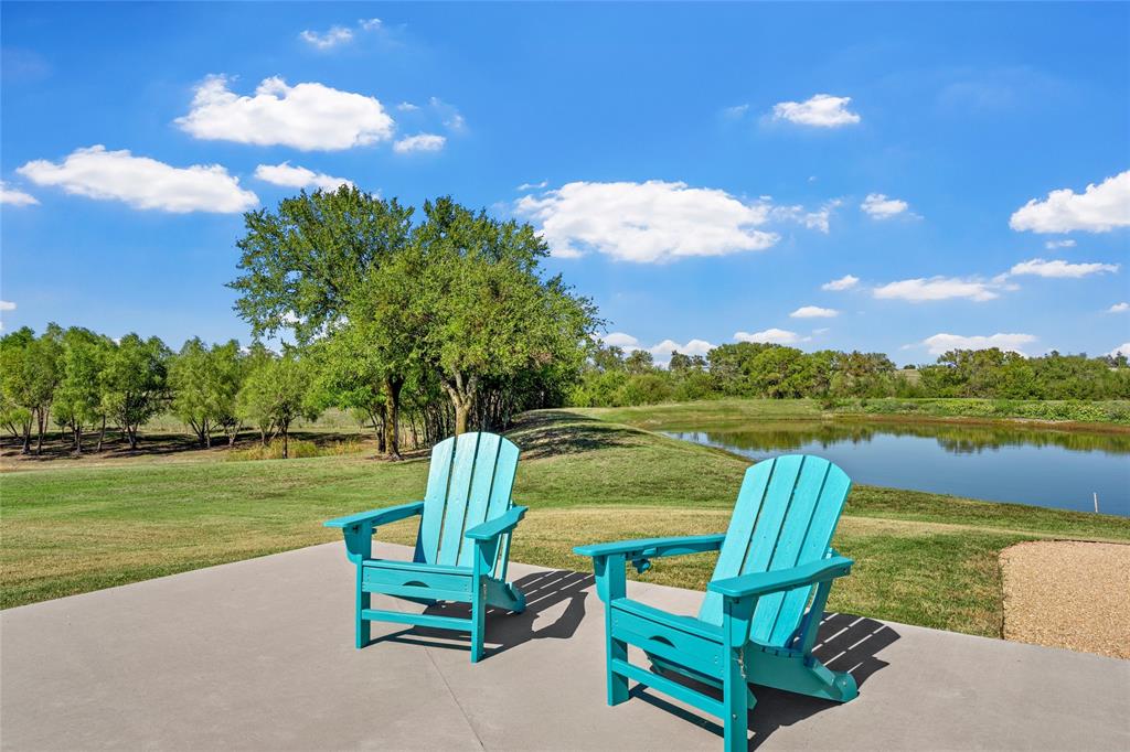 Concrete patio area with a pond frontage, manicured lawn, and mature perimeter trees
