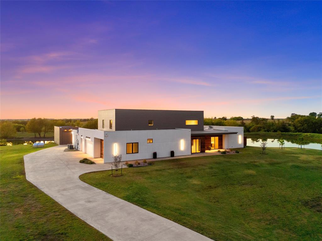 Modern two-story architectural exterior featuring smooth-finish cladding, expansive concrete driveway, flat roofing, and integrated wall-mounted exterior lighting