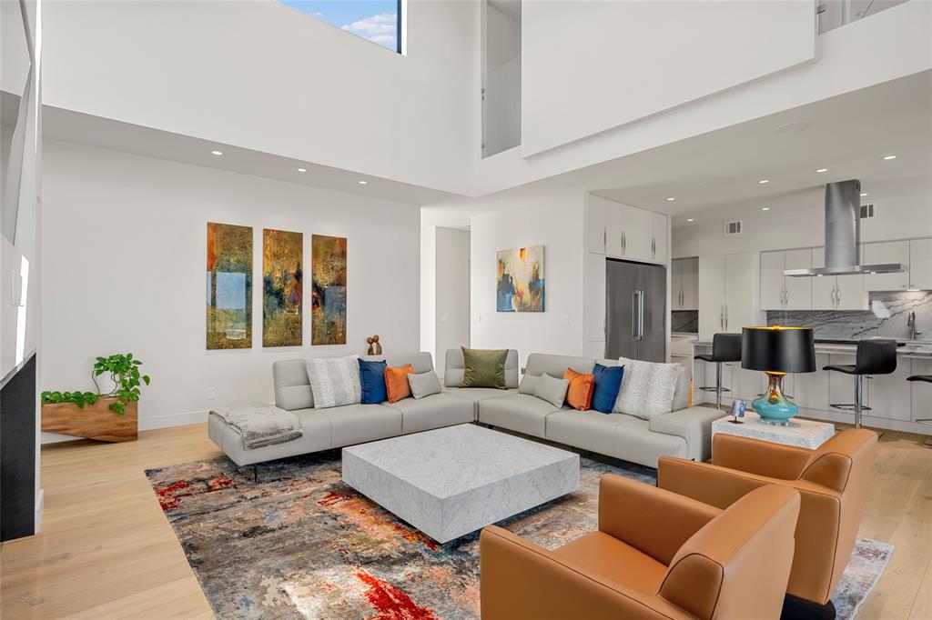 Open-concept interior featuring double-height ceilings, light wood flooring, recessed lighting, and a modern kitchen with integrated cabinetry and stainless-steel range hood