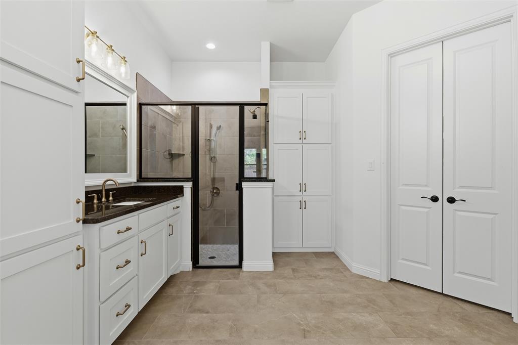 Bathroom featuring white cabinetry, dark countertops, a walk-in shower with a black frame and stone-look tiling, built-in floor-to-ceiling storage, and tile flooring