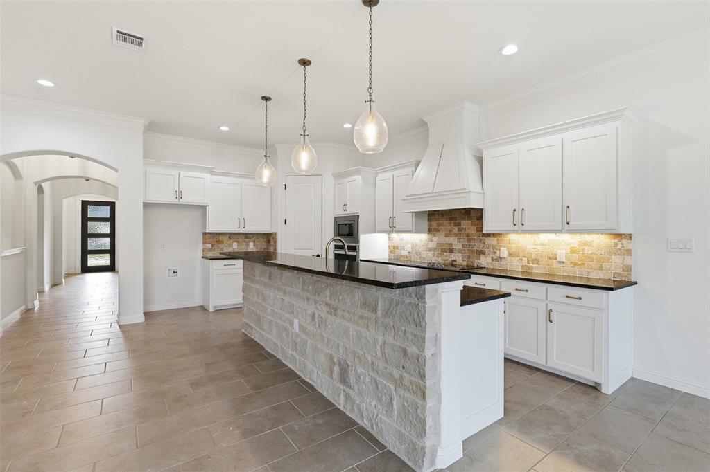 Kitchen featuring white cabinetry, a stone-faced breakfast bar with a dark countertop, a stacked stone backsplash, pendant lighting, and ceramic tile flooring