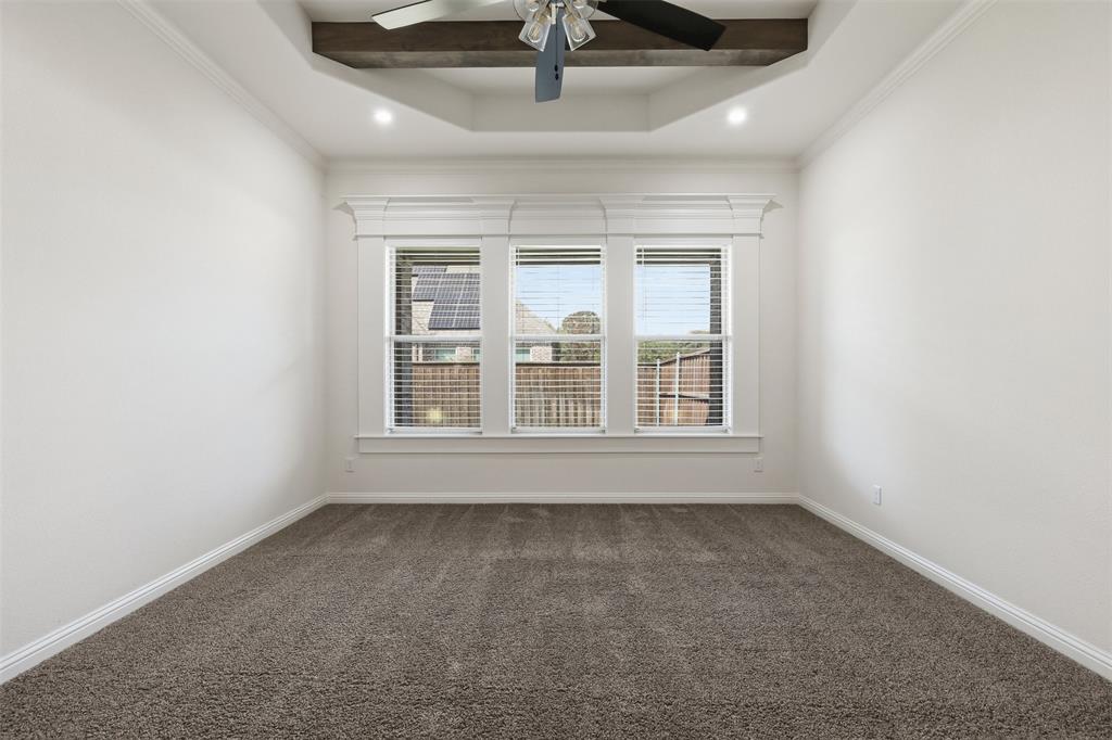 Tray ceiling featuring a stained wooden beam, plush carpeting, triple-window configuration with decorative casing, and a ceiling fan with integrated lighting