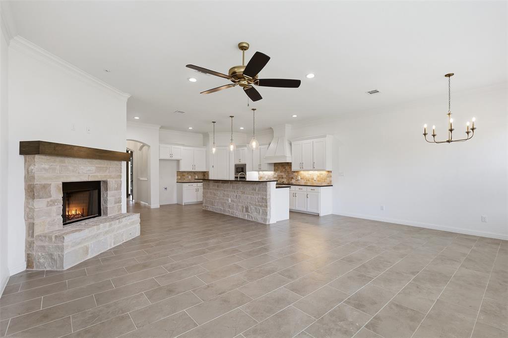 Open-concept area featuring stone-clad fireplace with wood mantel, stone-base kitchen island, custom white cabinetry, recessed lighting, and tile flooring