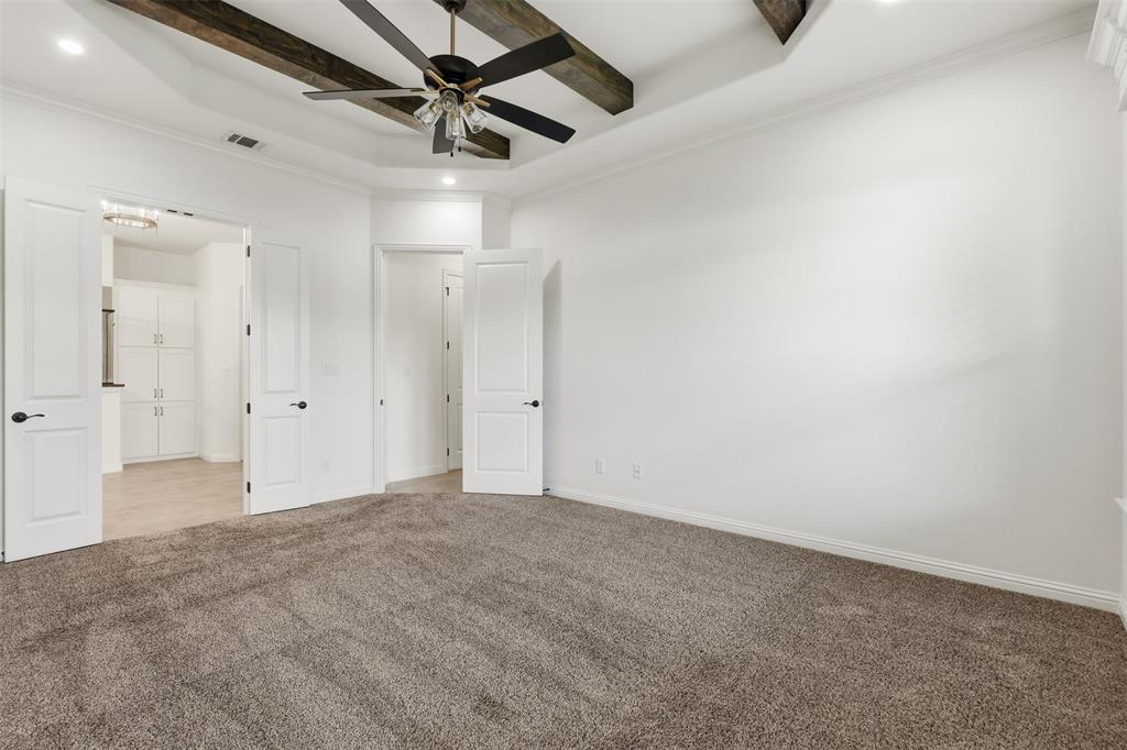 Tray ceiling featuring decorative stained wood beams, carpeted flooring, and a multi-blade ceiling fan with integrated lighting
