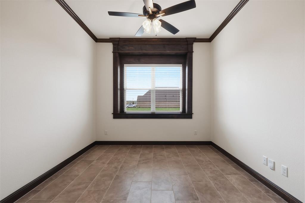 Room featuring large-format tile flooring, dark wood-finish crown molding, ceiling fan with integrated lighting, and a central window framed by matching dark wood-finish casing