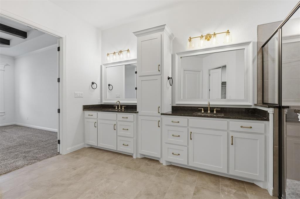 Double vanity featuring white cabinetry, a center storage tower, dark stone countertops, under-mount sinks, and framed mirrors with gold-tone wall-mounted lighting