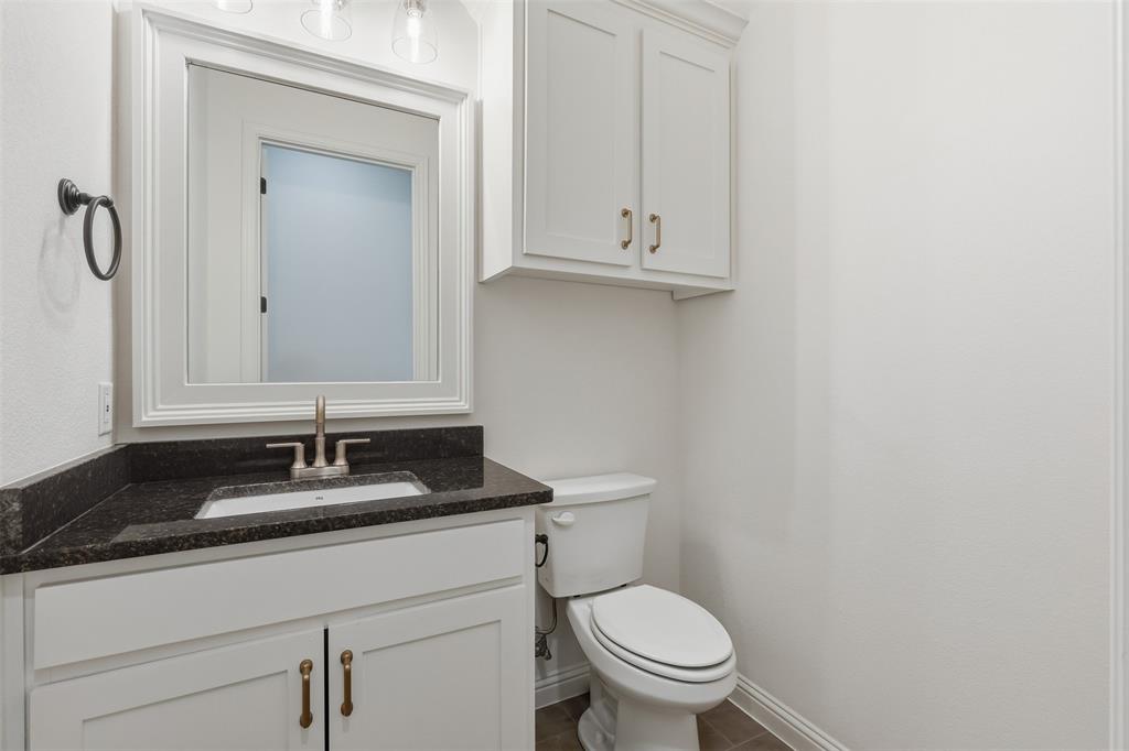 White shaker-style cabinetry with metallic hardware, dark stone countertop, undermount sink, matching wall-mounted cabinet, and framed mirror