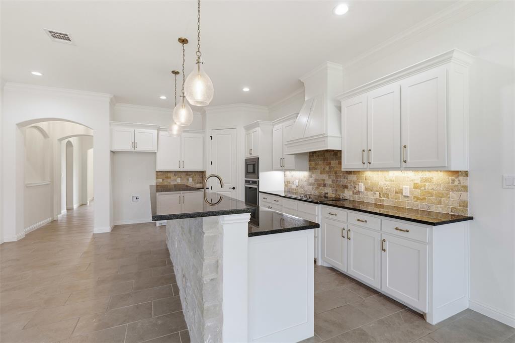 Kitchen featuring white shaker cabinetry, dark stone countertops, stone backsplash, built-in stainless steel appliances, and a central island with stone detailing