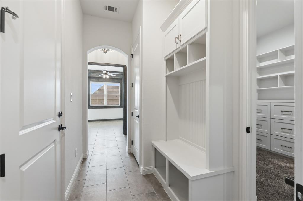 Built-in mudroom cabinetry with beadboard detailing, ceramic tile flooring, arched architectural passage, and custom closet storage with integrated shelving and drawers