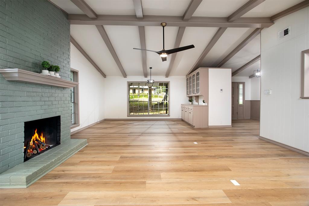 Painted brick fireplace with a wood mantel, exposed ceiling beams, wood-finish flooring, and built-in cabinetry with glass-front uppers