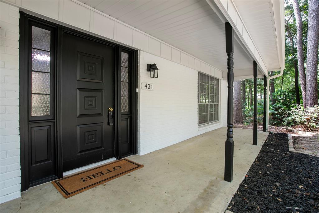 Covered front porch featuring a white painted brick facade, black paneled door with glass sidelights, and decorative turned support columns
