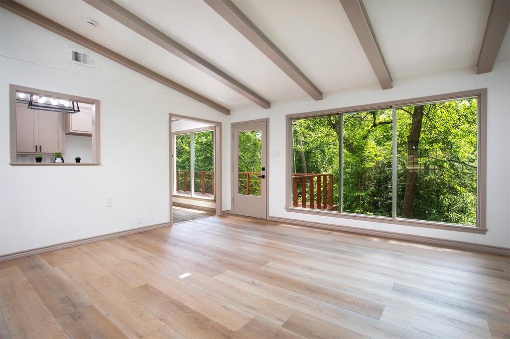 Living area featuring wood-finish flooring, exposed ceiling beams, expansive floor-to-ceiling windows, and a pass-through opening to the kitchen area