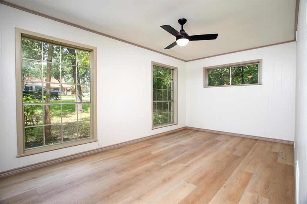Interior space featuring wood-finish flooring, white wall paneling, multiple grid-style windows, and a matte black ceiling fan with integrated light