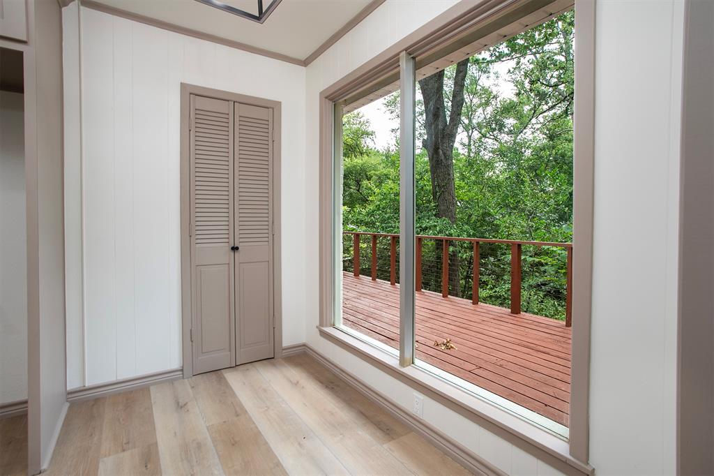 Wood-finish flooring, vertical paneling, louvered closet doors, and a large floor-to-ceiling window showcasing an exterior wood deck