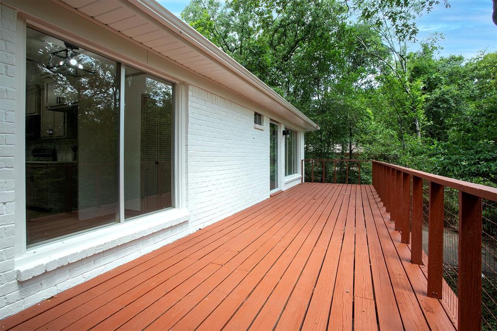 Painted brick exterior featuring an expansive wood deck with metal cable railing and sliding glass doors