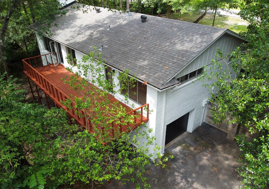 White brick exterior featuring an expansive wood deck, asphalt shingle roof, vertical siding accents, and a ground-level garage