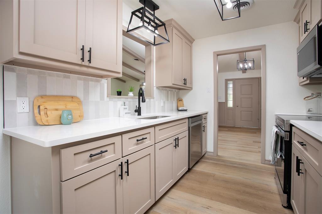 Kitchen featuring soft-tone cabinetry with matte black hardware, quartz countertops, a vertical-patterned tile backsplash, and geometric cage-style light fixtures