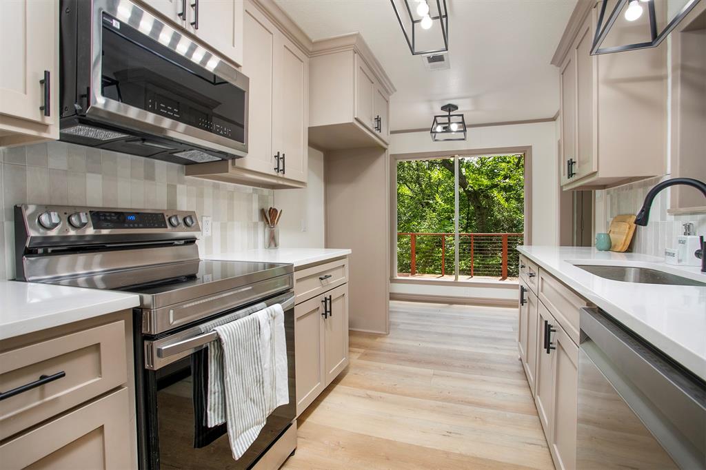 Kitchen featuring neutral-toned cabinetry, light-colored countertops, stainless steel appliances, wood-finish flooring, and geometric pendant lighting