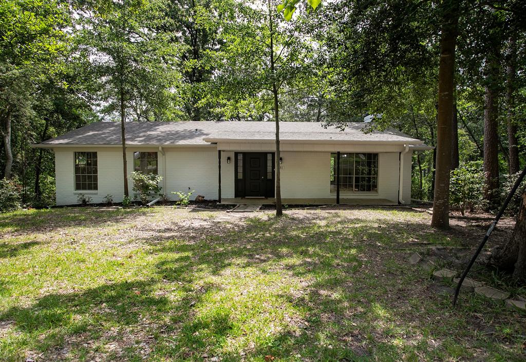 Single-story residence featuring white painted brick exterior, a covered front porch, multi-pane windows, and a mature tree-lined lot