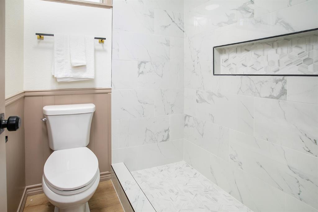 Walk-in shower featuring large-format stone-finish wall tile, a geometric-patterned inset storage niche, a mosaic-tiled floor, and wood-finish flooring