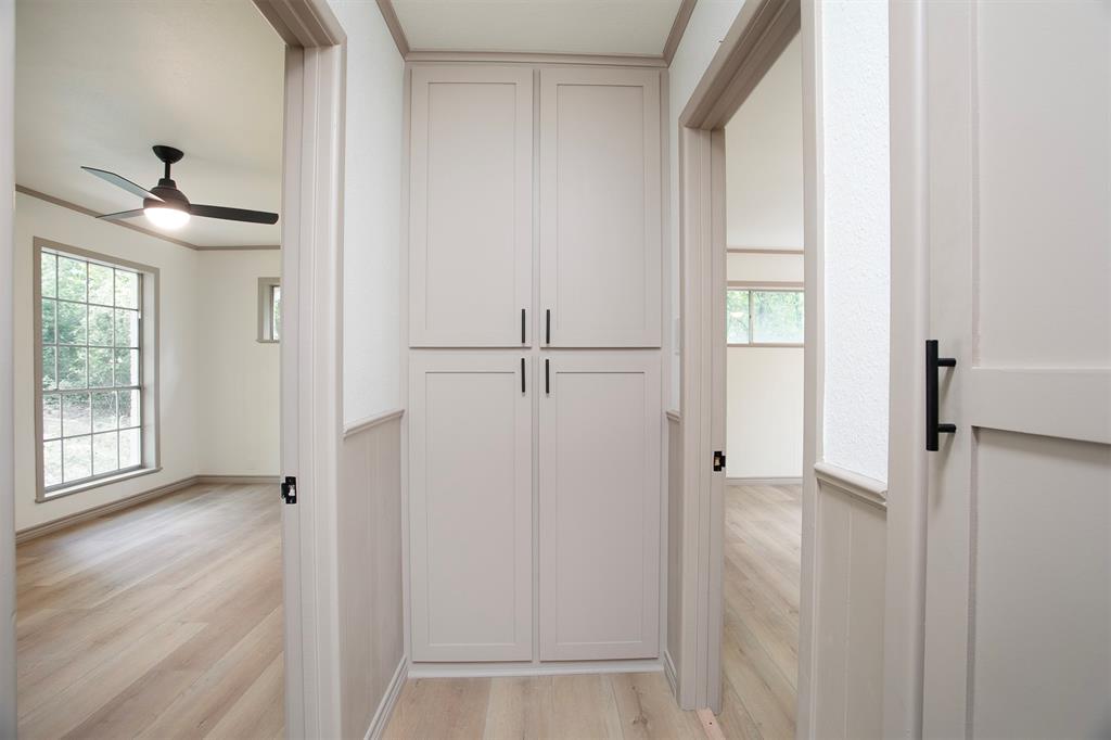 Hallway featuring floor-to-ceiling built-in cabinetry, wood-finish flooring, and shaker-style doors with matte black hardware