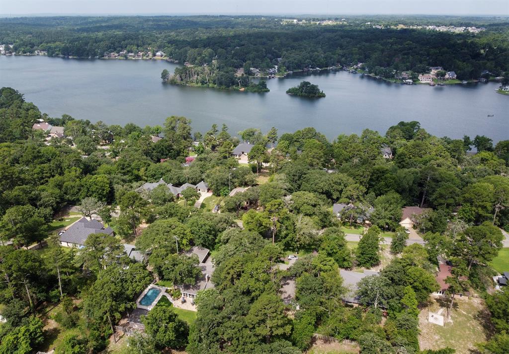 Aerial perspective featuring a residential lot with a private rectangular swimming pool, dense perimeter tree canopy, and direct proximity to a large inland lake
